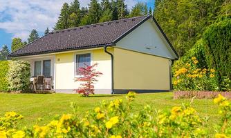 A beautiful yellow house with a garden full of flowers. In the background, green trees and a clear sky can be seen.