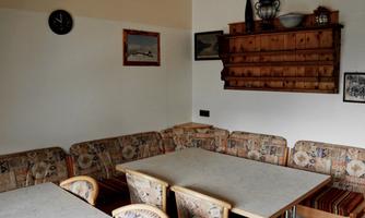 A simple, cozy dining room with a table and upholstered benches. On the wall, there are shelves and some pictures.