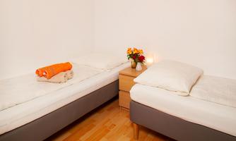 A simple bedroom with two single beds and a nightstand. On the nightstand are flowers and a small lamp.