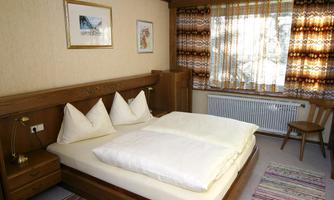 A cozy bedroom with a large bed and white pillows. The walls are adorned with warm wood tones and a larger window.