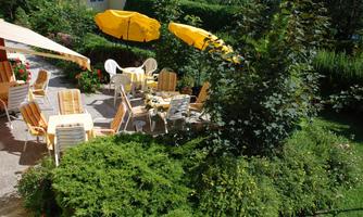 An inviting garden with yellow sun umbrellas and comfortable chairs. The surroundings are green and blooming, ideal for relaxed hours outdoors.