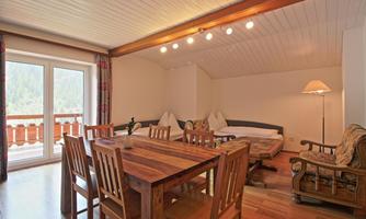 A cozy room with a wooden table and chairs. Large windows provide a view of the surrounding nature.