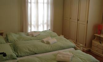 A cozy bedroom with three beds and bright green bed sheets. A wardrobe and a window with curtains create a bright atmosphere.