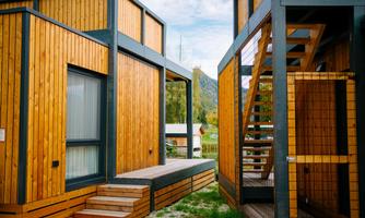 Modern wooden houses with clean lines and large windows. A staircase leads to one of the entrances, surrounded by a green landscape.