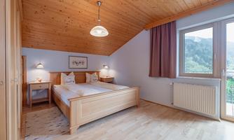 A cozy bedroom with two single beds and a wooden ceiling. Large windows let in plenty of light and offer a view of the surroundings.