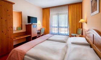 A bright room with two single beds and wooden furniture. Plenty of daylight comes in through the windows, and a beautiful view is visible.