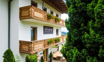 A charming building with wooden balconies and green plants. The surroundings are surrounded by trees and convey an inviting atmosphere.