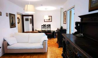 A bright living room with a white sofa and a wooden table. The floor is made of parquet and there are several pictures on the wall.