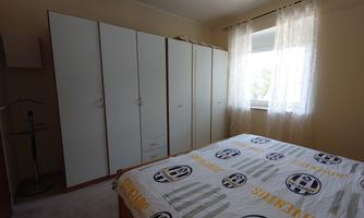 A simple bedroom with a bed and a large wardrobe. There is a window with curtains that lets in daylight.