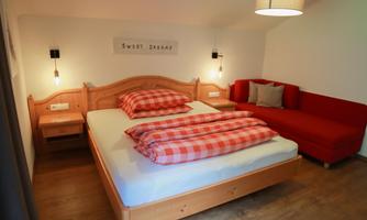 A cozy bedroom with a large double bed and red checkered bedding. Next to the bed is a red couch, and the room is designed in warm tones.