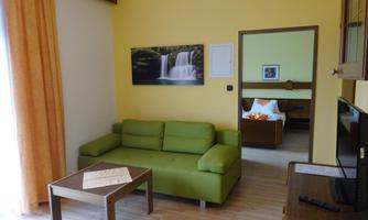 A cozy living space with a green sofa, a coffee table, and a TV corner. On the wall hangs a picture of a waterfall.