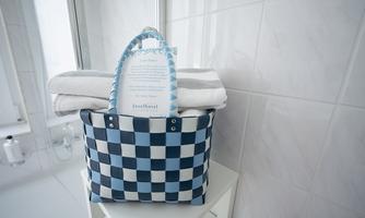A braided basket in blue and white stands on a table. Inside are two towels and an information card.