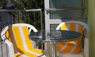 A small balcony with a round table and two chairs. The chairs are upholstered with yellow stripes and it is a sunny day.