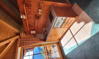 A friendly kitchen with wooden shelves and a small cooking area. The light impressively pours through the window and illuminates the space.