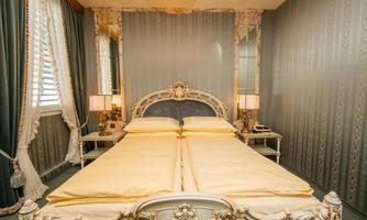 An elegant bedroom with a large, royal bed and soft lighting. The walls are decorated in a classic style with fine curtains.