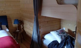 A cozy wooden room with two beds. A blue lamp and a red bed sheet create an inviting atmosphere.