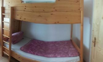 A wooden bunk bed in a bright bedroom. The room has light walls and a warm wooden floor.
