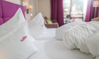 A modern hotel room with a comfortable bed and white pillows. The decorative purple curtains create a cozy atmosphere.