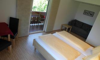 A cozy bedroom with a double bed and a sofa. The room has access to a balcony with a view of the outdoors.