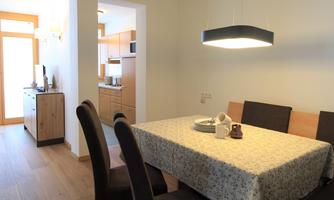 A bright dining area with a large table and elegant chairs. In the background, a modern kitchen is visible.