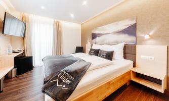 A modern hotel room with a large bed, a television, and an elegant wooden design. Large windows allow plenty of daylight in.