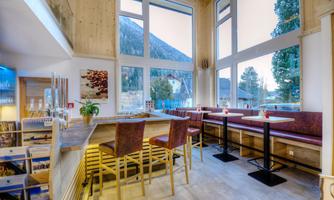 A modern café with large windows and a view of the mountains. The decor is bright and inviting, with wooden details and cozy seating.