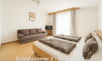 A modern bedroom with a double bed and a comfortable sofa. Large windows provide plenty of daylight.