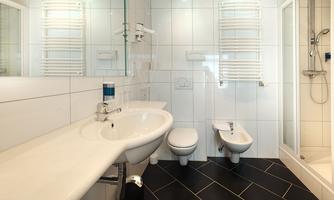 A modern bathroom with white tiles and elegant sanitary ceramics. There is a shower, a sink, and a bidet.