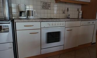 A modern kitchen with bright cabinets and a granite countertop. Featured are a stove, a dishwasher, and a coffee machine.