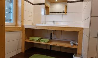 A modern bathroom with white tiles and wood paneling. Green towels are on the countertop and a mirror is above the sink.