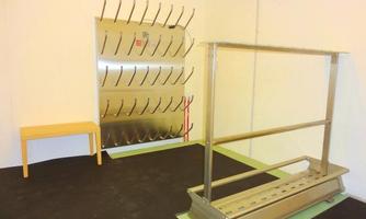 A simple room with a metal wall for hanging and a stand in the center. On the left, there is a small table.