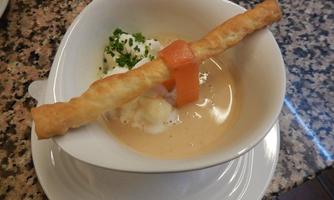 A creamy soup with a crispy dough strip and a piece of salmon. Fresh herbs decorate the dish.