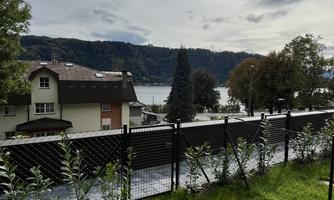 A peaceful landscape with a view of a lake and rolling hills. The foreground is designed with green grass and a black fence line.