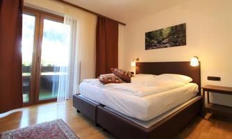 A cozy bedroom with a large double bed and soft wooden tones.  
Large windows provide plenty of daylight and a pleasant atmosphere.