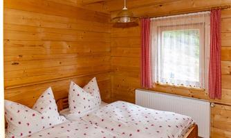 A cozy bedroom with wood paneling and a double bed. The windows with checked red curtains let in plenty of light.