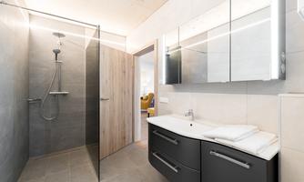 A modern bathroom with a walk-in glass shower. The walls are bright and stylish, and there is a practical washing area with plenty of storage space.
