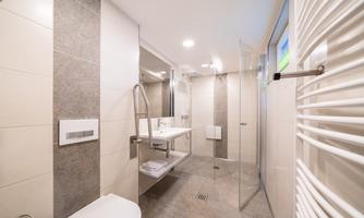A modern bathroom with a spacious shower and bright tiles. The furnishings are simple and elegant, featuring a vanity and towel holders.