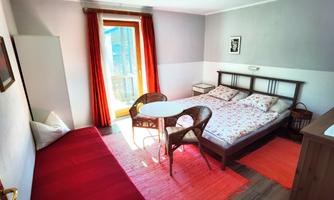 A simple room with a double bed and a single bed. There is a table, chairs, and large windows with red curtains.