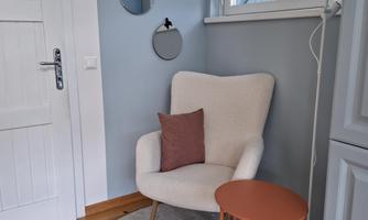 A cozy armchair with a decorative cushion stands next to a small table. Two round mirrors hang on the wall, and the floor is covered with a round rug.