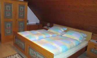 A cozy bedroom with a wooden bed and colorful bedspreads. In the room, there is a wardrobe and a bedside lamp.