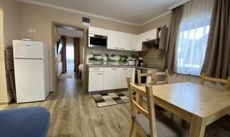 A modern kitchen with wooden flooring and a dining table. The room is bright and friendly, with a window and modern appliances.