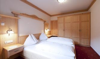 A cozy bedroom with two single beds and wooden-paneled walls. The room has a warm and inviting character.