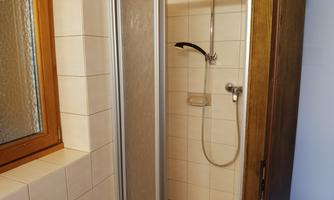 A modern shower in a bright bathroom. The walls are tiled, and there is a large window for daylight.