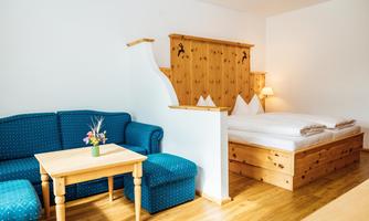 A cozy room with a wooden bed and a blue couch. There is a small table with a vase of flowers in the middle.