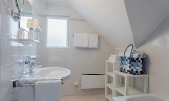 A bright bathroom with white tiled walls and a sink. Towels and toiletries are neatly arranged.