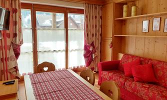 A cozy living area with a red sofa and wooden shelves. Large windows let in a lot of light, and the curtains have a heart-shaped pattern.