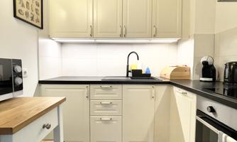 A modern kitchen with white cabinets and an elegant wooden countertop. The amenities include a stove, a microwave, and a coffee machine.