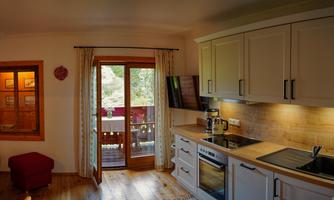 A modern kitchen with bright cabinets and wooden countertops. The room has large windows overlooking a balcony.