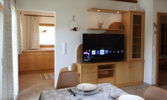 A bright and inviting living room with a television and a dining table. The kitchen is visible in the background, creating a cozy atmosphere.