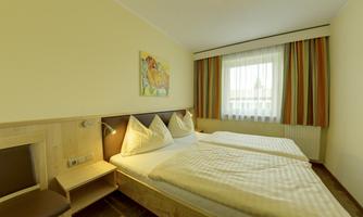 A bright hotel room with two single beds and colorful curtains. A colorful picture hangs on the wall.